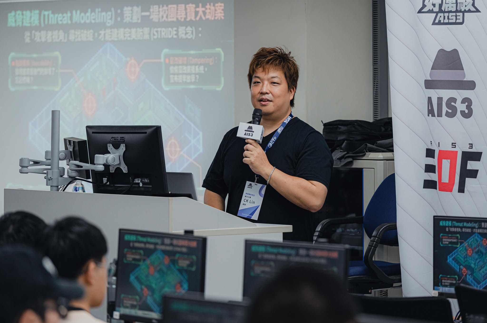 CK Lin lecturing on threat modeling (STRIDE) at the AIS3 2026 main course, with students following along on lab machines